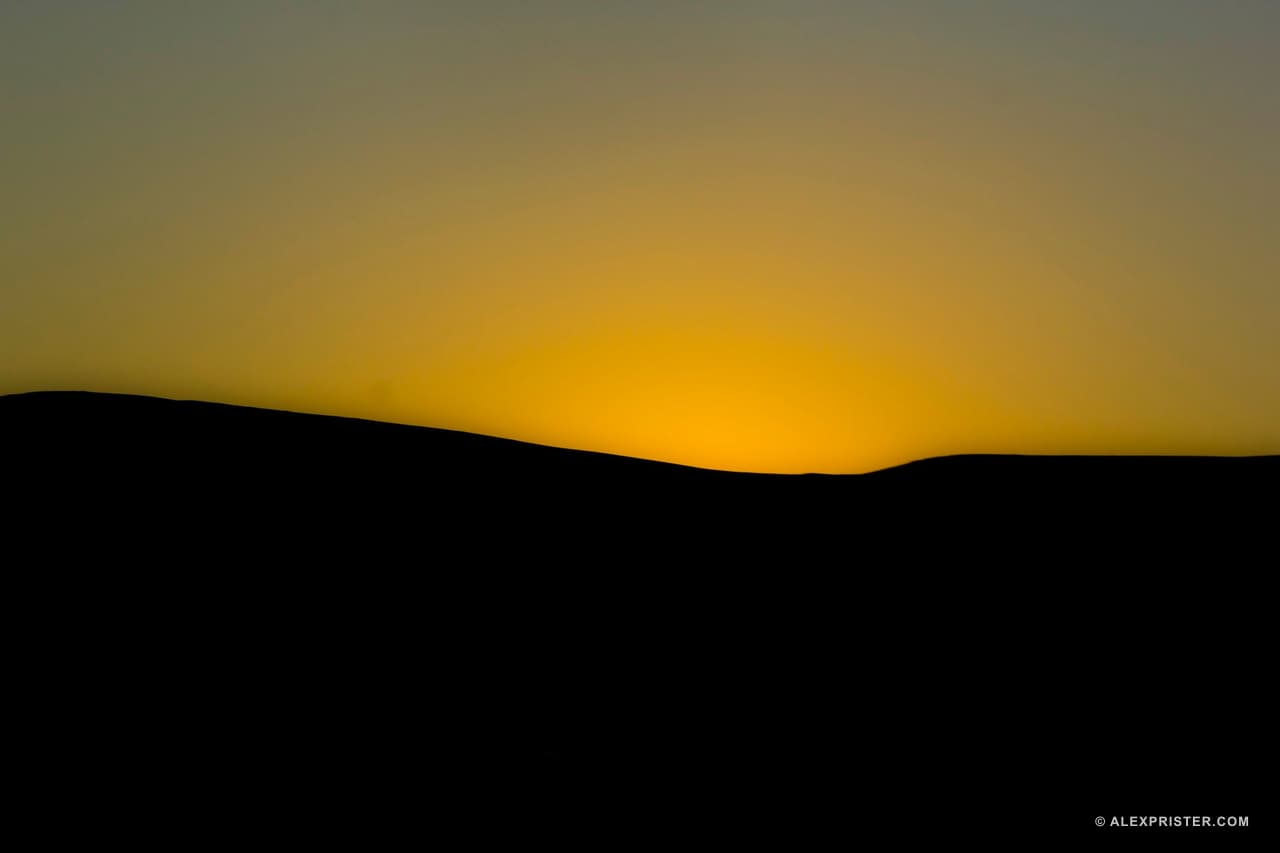 A black desert ridge silhouetted below a clean band of amber sky