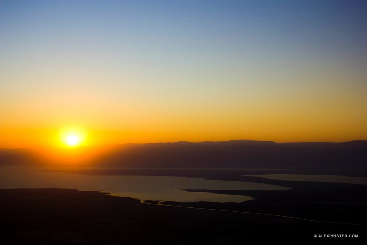 The sun rising over a distant desert horizon and reflective water